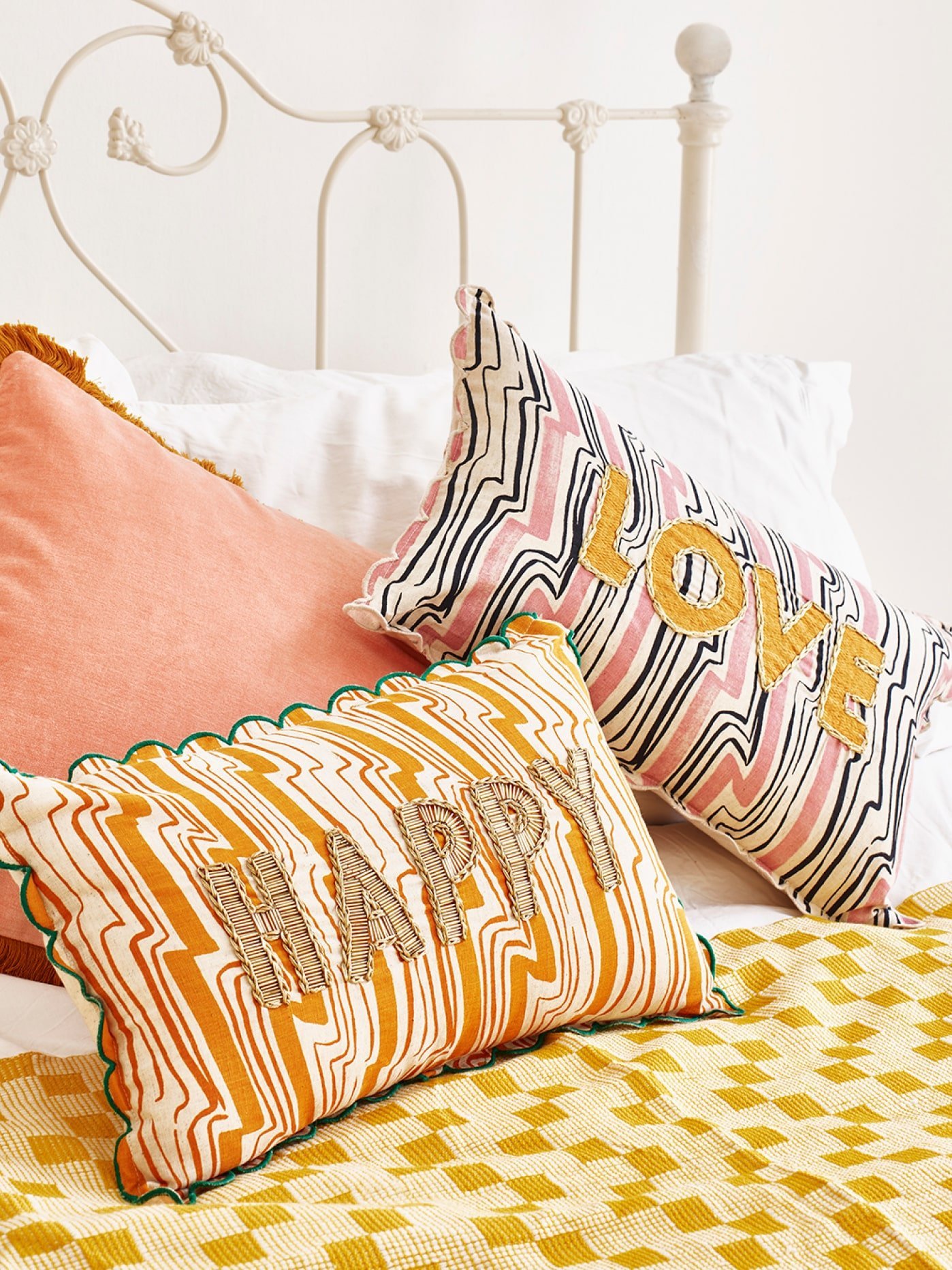 Three patterned cushions on a white bed with yellow throw