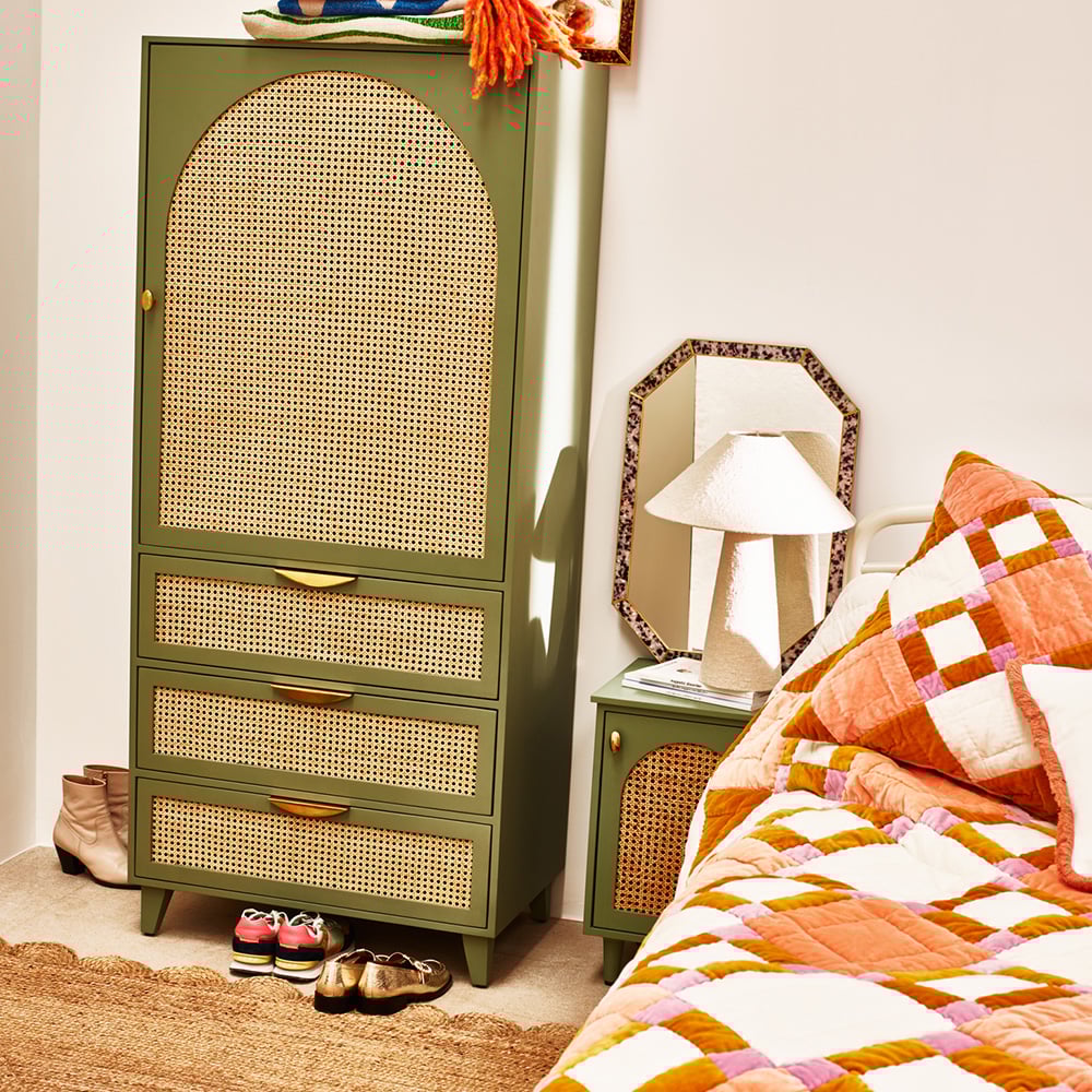 A bed with a patchwork bedspread, next to a wardrobe and table light 